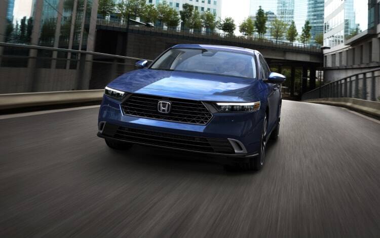 2025 Honda Accord Touring Hybrid in Canyon River Blue Metallic driving down a city street, showing the stylish grille and front end.